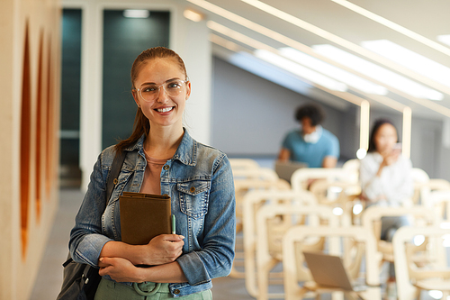 Portrait of smiling confident beautiful girl in eyeglasses holding notepad in lecture room