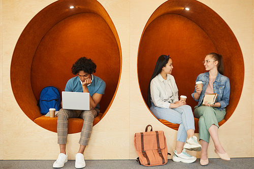 Modern multi-ethnic students sitting in comfortable wall chairs and resting during break at university