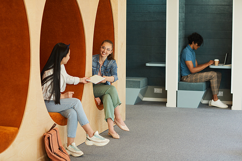 Smiling student girl passing lecture notes to group mate while they sitting in cozy university hall