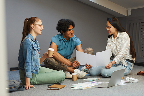 Asian student girls sitting on floor and showing papers while discussing charts with group mates