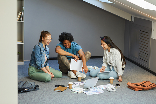 Group of interracial students studying economics students brainstorming about project together using laptop and charts