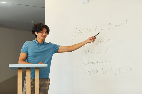 Content confident mixed race student boy pointing at whiteboard while explaining math solution at university class