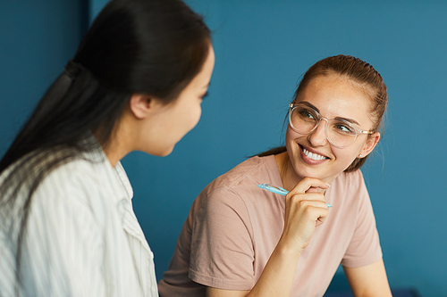 Smiling student girl in eyeglasses holding pen and discussing project ideas with groupmate