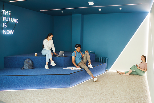 Group of multi-ethnic modern students sitting in campus lobby and preparing for exam