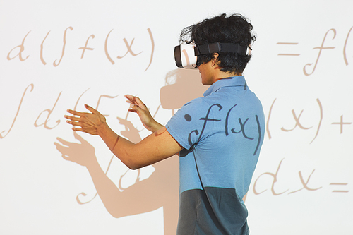 Rear view of mixed race student boy gesturing hands while analyzing math calculations in VR device