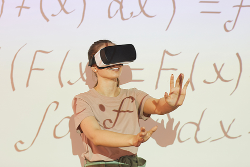 Positive student girl in VR goggles gesturing hands while solving math problem, she enjoying virtual education