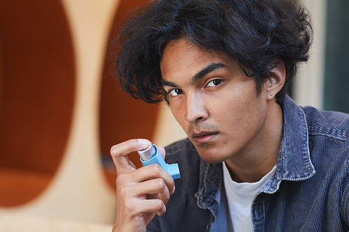 Portrait of mixed race boy suffering from asthma using inhaler during asthma attack at university