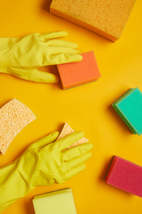 Close-up of woman in rubber yellow gloves using sponges for cleaning isolated on yellow background