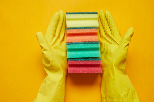 Close-up of woman in rubber gloves holding colorful sponges in a row isolated on yellow background