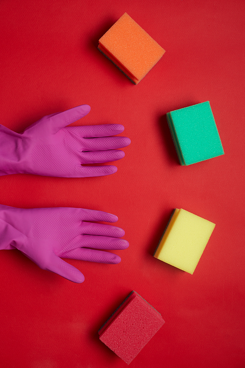 High angle view of rubber gloves and colorful sponges isolated on red background