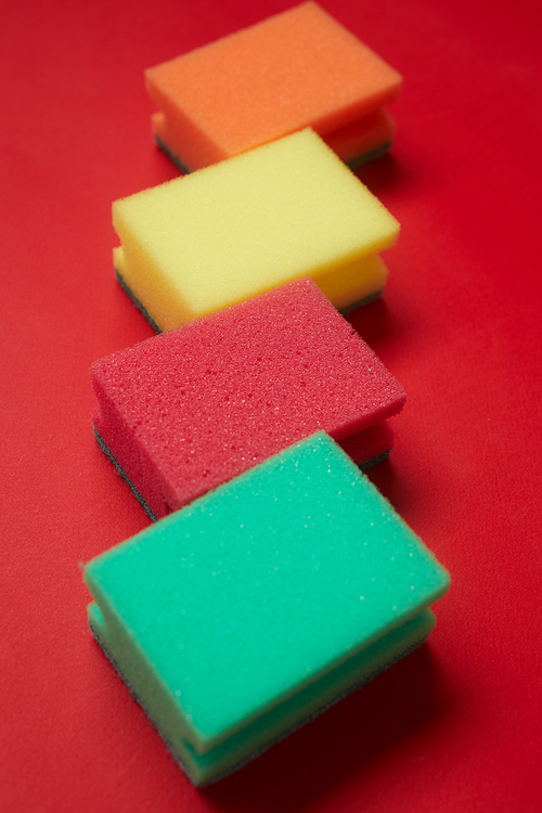 Close-up of colorful sponges for cleaning lying in a row isolated on red background