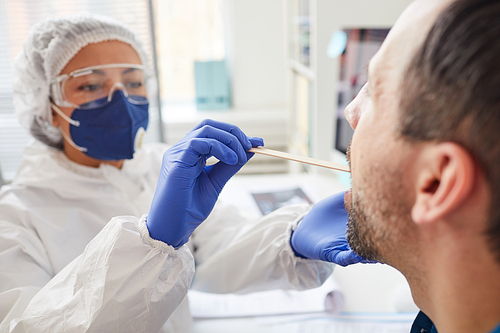 Mature man opening the mouth while doctor in protective clothing examining his throat during medical exam at hospital