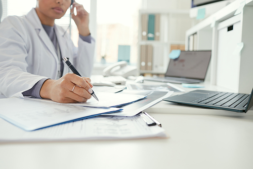 Close-up of female doctor sitting at the table and filling the documents at office