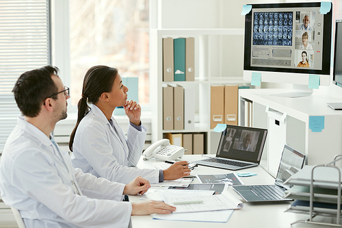 Doctor and nurse sitting at the table and listening to their colleagues on computer monitor they have online conference