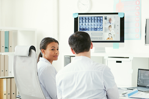 Two doctors talking to each other while sitting at the table and examining x-ray images at office