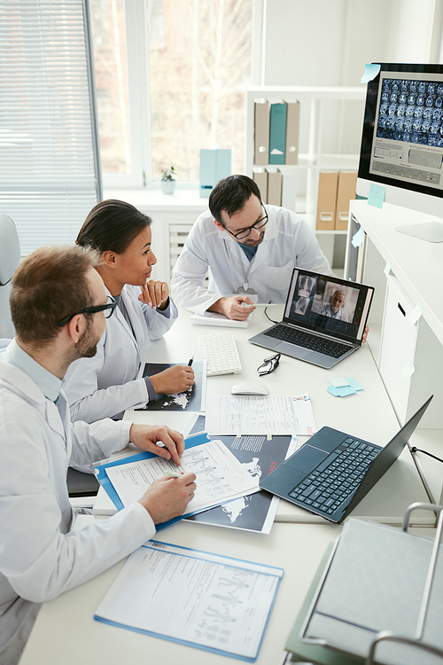 Group of doctors sitting at the table and talking to their colleague during online conference at meeting