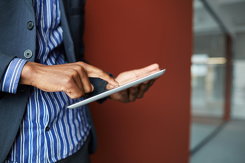 Close-up of African man in suit standing and typing on digital tablet