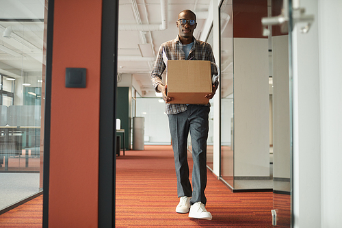 African young man carrying box with things while walking along the office corridor he getting a new job