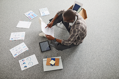 High angle view of African businessman sitting on the floor and examining business charts and graphs