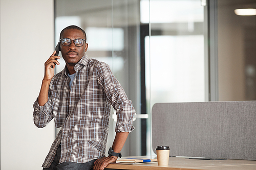 African businessman in eyeglasses has a conversation on mobile phone while sitting at office