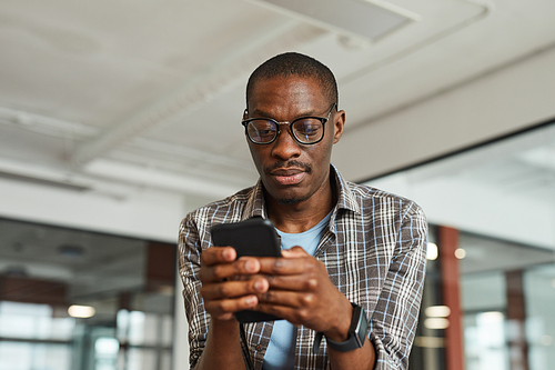 African designer in eyeglasses using his mobile phone for online work