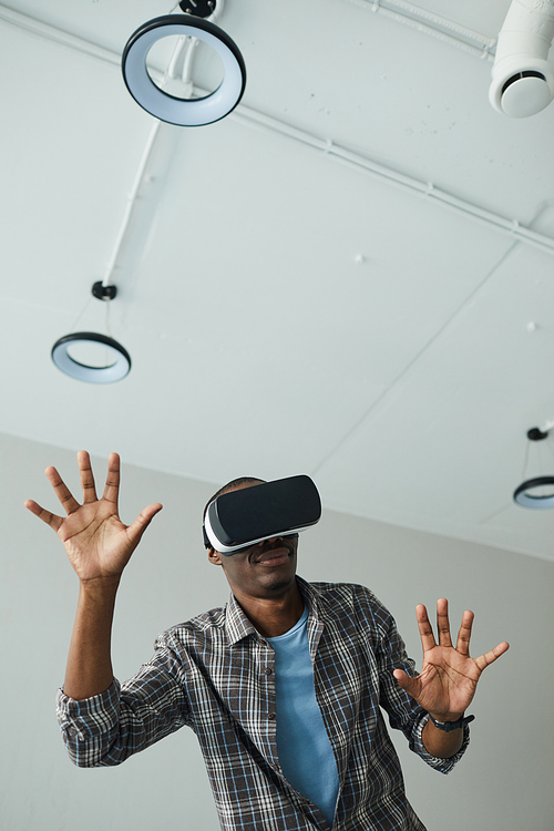 African guy in special glasses gesturing he playing in virtual reality game in the room