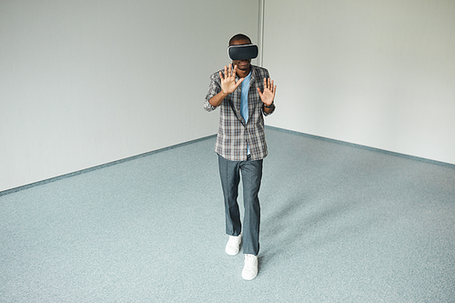 African young man in casual clothing wearing virtual glasses playing in game in empty room