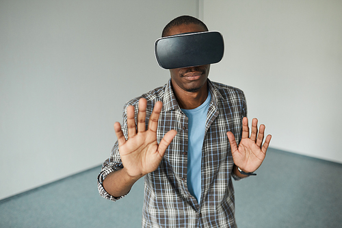 African young man in virtual reality goggles gesturing during the game he is in empty room