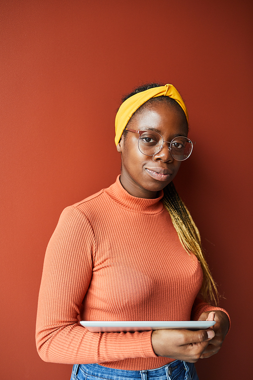 Portrait of African young woman with beautiful hairstyle holding digital tablet and looking at camera isolated on brown background