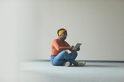 African young woman sitting on the floor in empty room and using digital tablet she working online