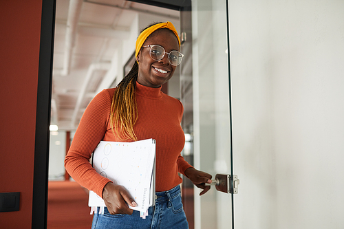 Portrait of African young businesswoman smiling at camera while going into the office at meeting