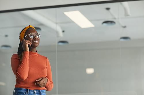 African young woman in eyeglasses talking on mobile phone while standing at office