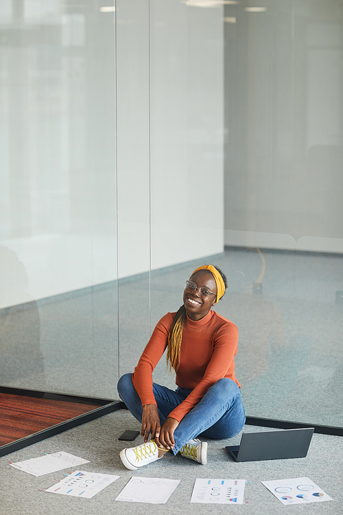 African businesswoman sitting on the floor with laptop and business documents and working in empty modern office