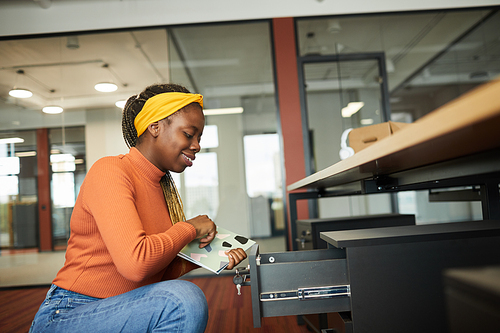 African smiling businesswoman getting folders from the box of her desk while working at office