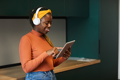 African happy designer wearing wireless headphones typing on digital tablet she working online at office