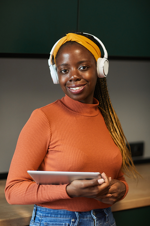 Portrait of African woman in wireless headphones smiling at camera while using digital tablet