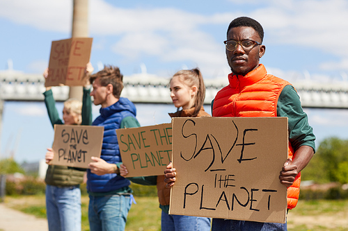 Portrait of African man holding placard Save the planet and looking at camera with his friends in the background