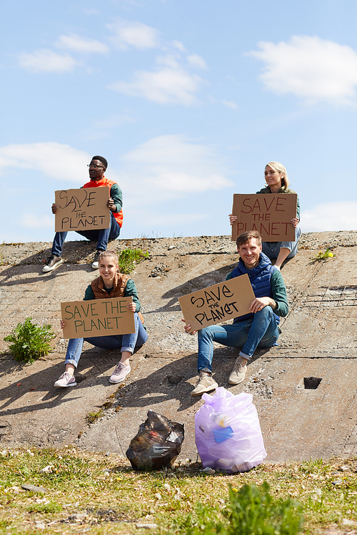Group of young volunteers sitting on the rock with cardboard placards outdoors