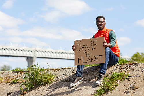 Portrait of African young volunteer sitting on the ground with placard outdoors