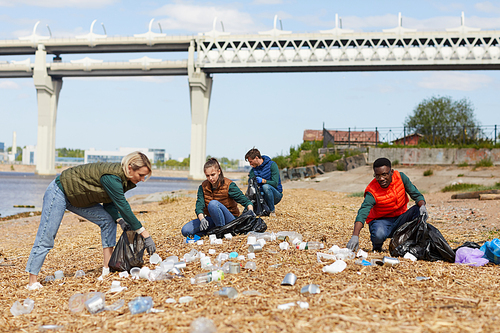 Group of volunteers picking up the garbage near the bank of the river outdoors