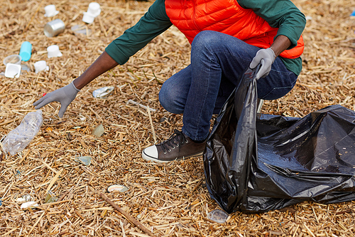 Close-up of young woman picking up the garbage into the bag outdoors
