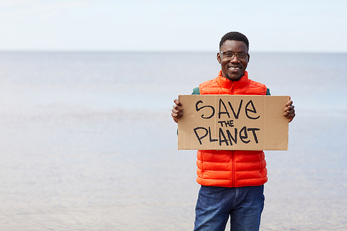 Portrait of African young man holding placard Save the planet and smiling at camera while standing outdoors