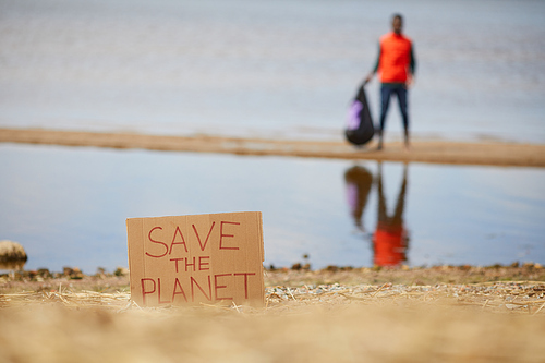Image of placard Save the planet on the beach of the sea with man standing in the background