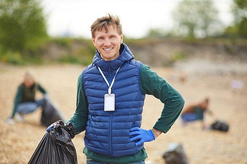 Portrait of young man holding bag with garbage and smiling at camera while standing outdoors