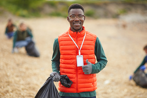 Portrait of African young man holding bag with garbage and smiling at camera while standing outdoors