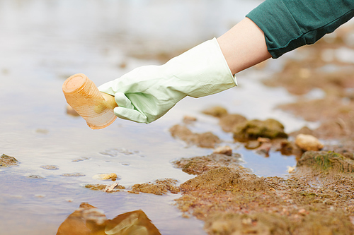 Close-up of woman in protective gloves picking up the rubbish on the river