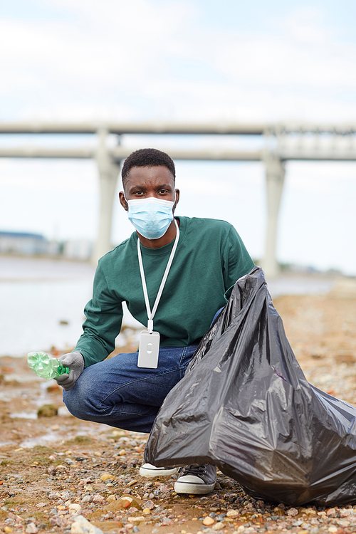 Portrait of African young volunteer putting rubbish in bag and looking at camera while working in the city
