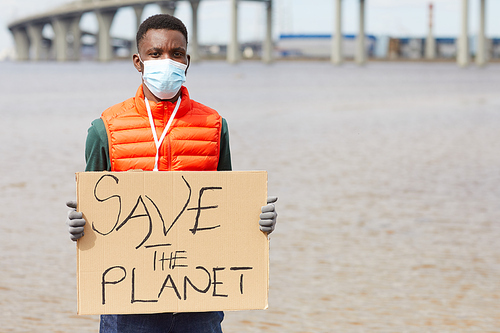 Portrait of African young man in protective mask holding placard and looking at camera while standing near the coastline