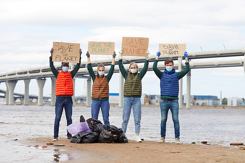 Group of volunteers raising placards up standing near the rubbish bags near the coastline