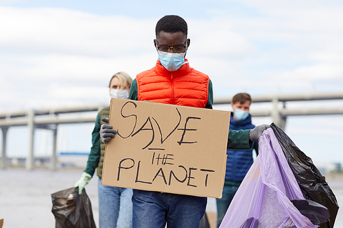 African young man in protective mask holding placard with other volunteers working in the background outdoors